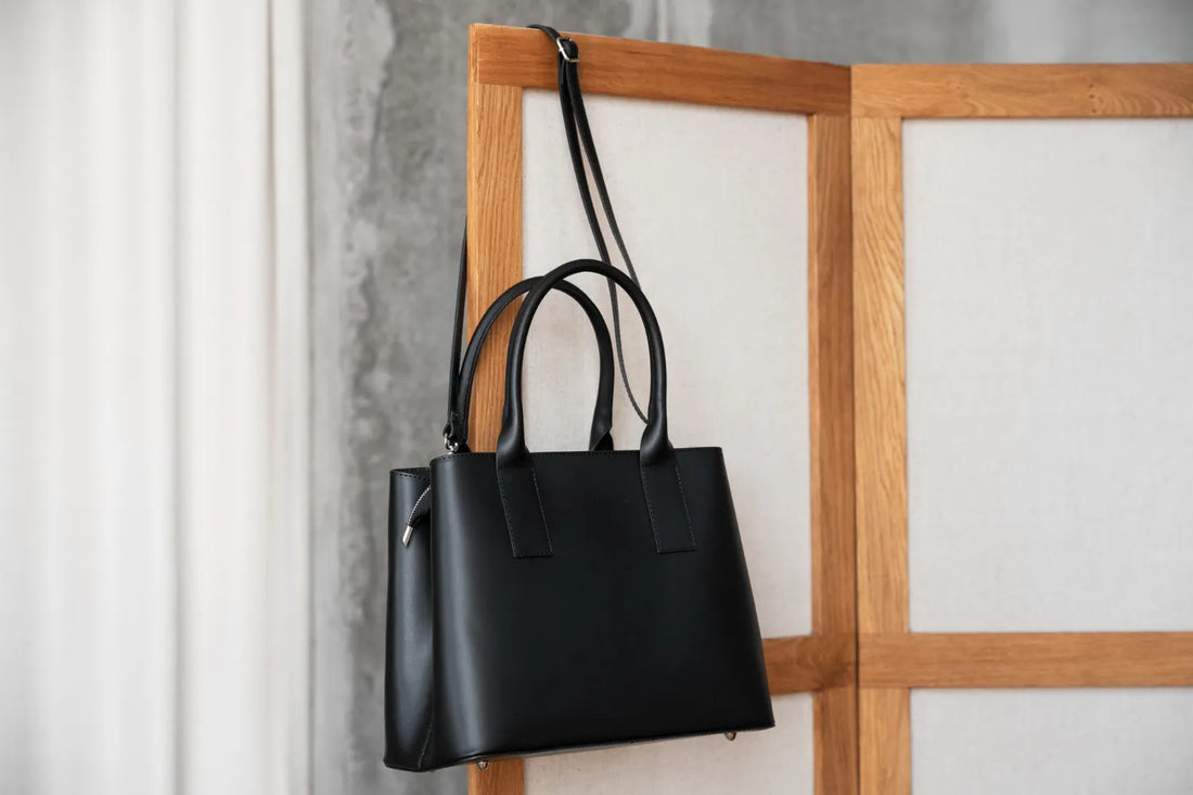 Black leather tote bag hanging on a wooden frame.