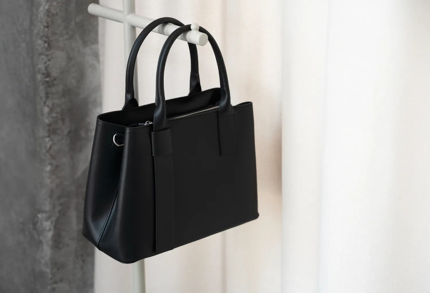 Black leather tote handbag hanging on a rack.